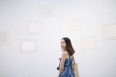 Portrait of young woman standing against wall at home