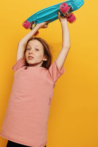 Portrait of young woman with arms raised standing against yellow background