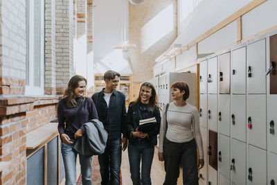 Male and female students talking while walking in school corridor