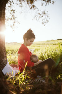 Side view of breast feeding baby while sitting on field