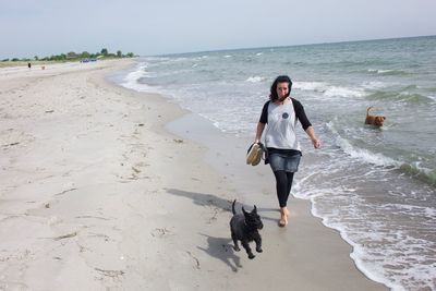 Full length of mature woman with dogs walking on shore at beach