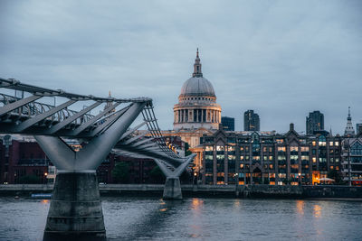 Bridge over river in city against cloudy sky