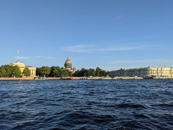 View of buildings by river against blue sky