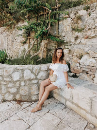 Young woman in white summer dress sitting on stone bench.