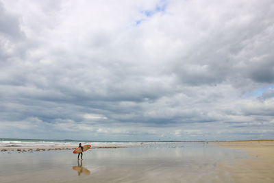 Rear view of woman walking at beach against cloudy sky