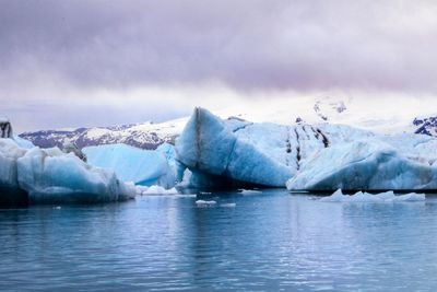 Scenic view of icebergs melting in sea against cloudy sky