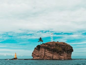 Lighthouse on rock by sea against sky