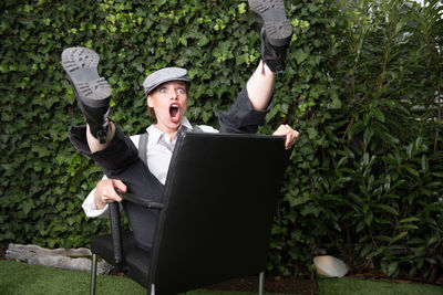 Woman making funny faces while sitting on chair against plants