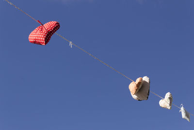 Low angle view of heart shape cushions hanging on rope against clear blue sky