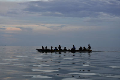 Boats in calm sea against cloudy sky