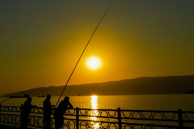 Silhouette man fishing in lake against sky during sunset