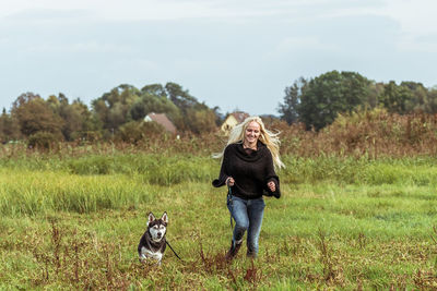 Portrait of woman with dog standing on field against sky