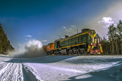 Train on railroad tracks by snowy field against sky
