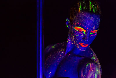 Woman wearing neon clothing by pole against black background