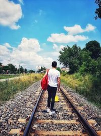 Rear view of man standing on railroad track against sky