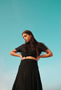 Low angle view of woman standing against clear blue sky