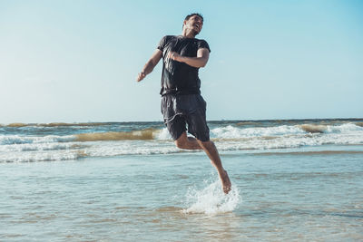 Full length of cheerful man jumping over sea against clear sky