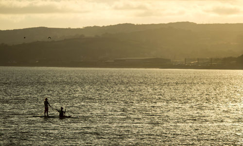 Silhouette people on sea against sky during sunset