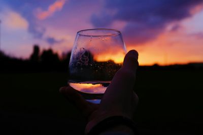 Hand holding wine glass against silhouette landscape