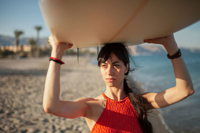 Woman carrying surfboard while walking at beach