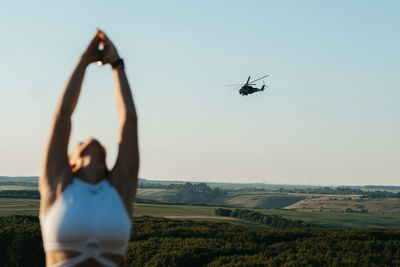 Woman meditating and practicing yoga outdoors at sunset and combat helicopter on the background	
