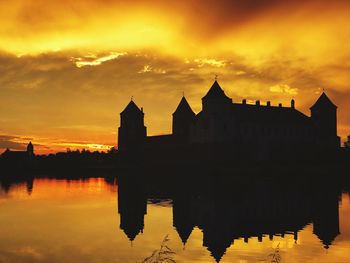 Silhouette of buildings by lake against orange sky