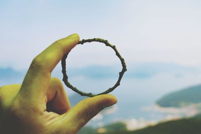 Close-up of hand holding leaf against sky