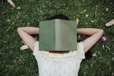 High angle view of woman lying on grass with book on face