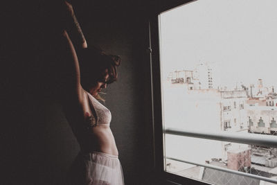 Side view of woman stretching by window at home