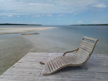 Chair on shore at beach against sky