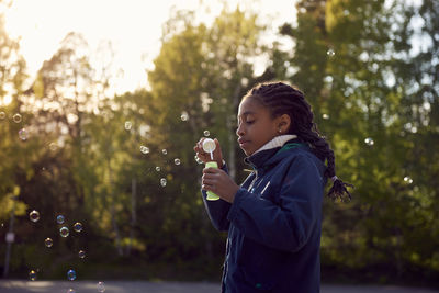 Side view of girl holding bubble wand against trees at campsite