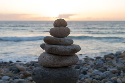 Stack of pebbles on beach against sky during sunset