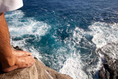 Low section of man standing by sea on rock during sunny day