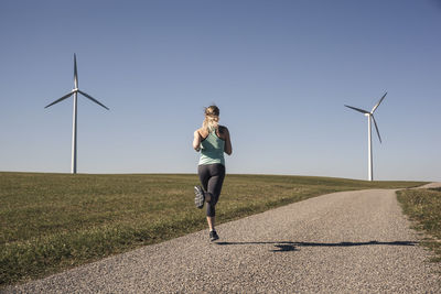 Young woman jogging on field way, wind wheels in the background