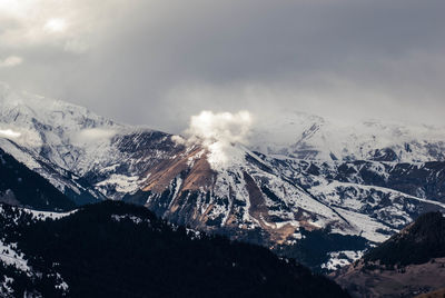 Smoke erupting from snow covered mountains against cloudy sky