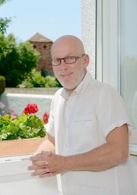 Portrait of man standing against window at home