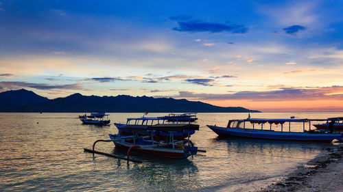 Boats moored in sea against sky during sunset