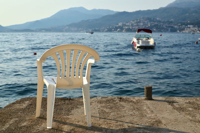 White plastic chair on a beach with a view to a sea and a boat