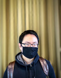 Portrait of young man wearing eyeglasses and face mask against wall.