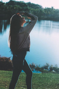 Side view of woman standing on field by lake during sunny day