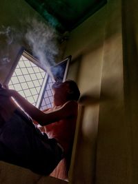 Side view of man sitting by window at home