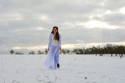 A young woman wearing a white corset dress is running in nature, on a  winter day, with lots of snow