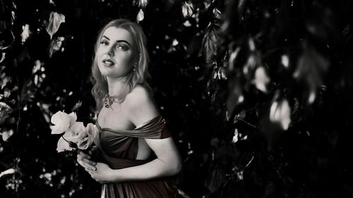 Portrait of young woman standing against trees