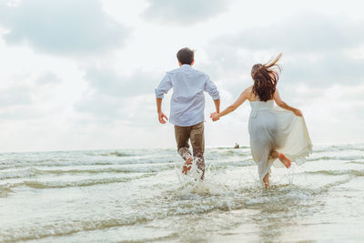 Rear view of couple holding hands running on beach