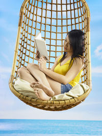 Side view of a smiling young woman sitting against sky