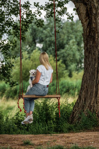 Young woman with a white dog on a tree swing.