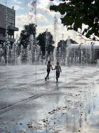 People on fountain in city against sky