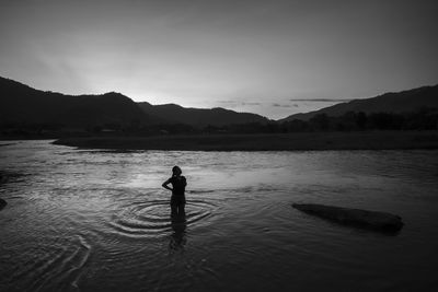 Silhouette man standing in lake against sky