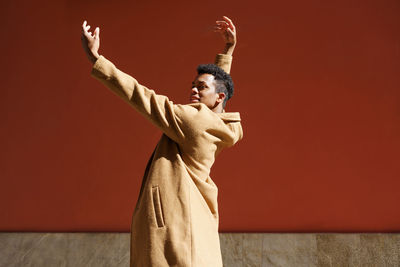 Smiling man dancing against red wall