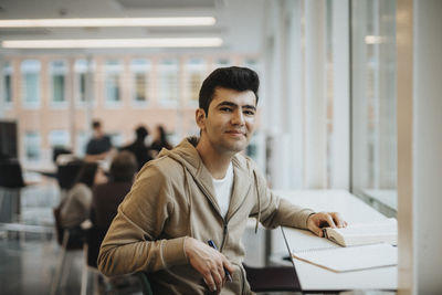Portrait of smiling male student sitting at table in university